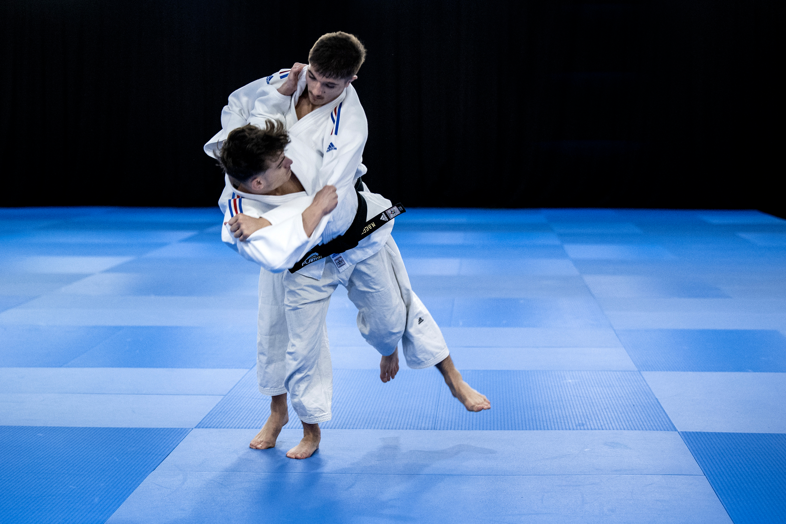 Un binôme de judokas en pleine exécution d'une technique hane-goshi sur un tatami bleu